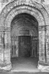 Black & white shot of a side entrance into Dunfermline abbey. The entrance is comprised of an old wooden door and stone archway.