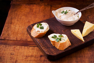 Composition with tasty baguette sandwiches and savory cream on a wooden table