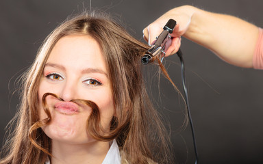 Stylist curling hair for young woman.