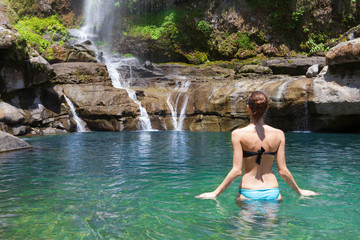 Fototapeta premium Woman going for a swim in a tropical waterfall spring setting.
