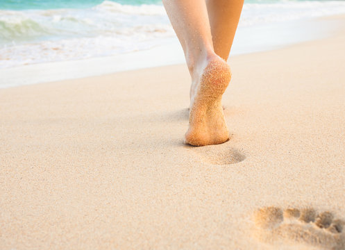 Beach travel - woman walking on sand beach leaving footprints in the sand.