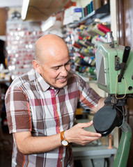 Mature  workman sewing leather boots on stitch lathe