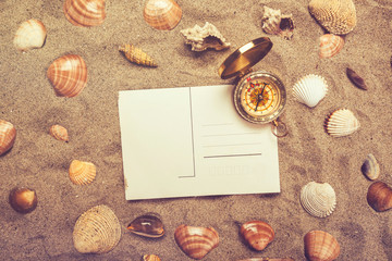Blank postcard in hot beach sand and compass