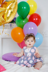 Fototapeta na wymiar Portrait of a little redheaded girl with gray eyes,pink bow on its head, in a beautiful dress on a background of Golden stars and colorful balloons, posing in her first birthday on white background