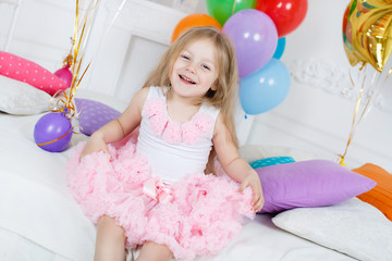 Obraz na płótnie Canvas Little girl with long straight hair, with a pink bow on her head, dressed in a pink and white dress on gray background with colorful balloons and gold stars to your fourth birthday