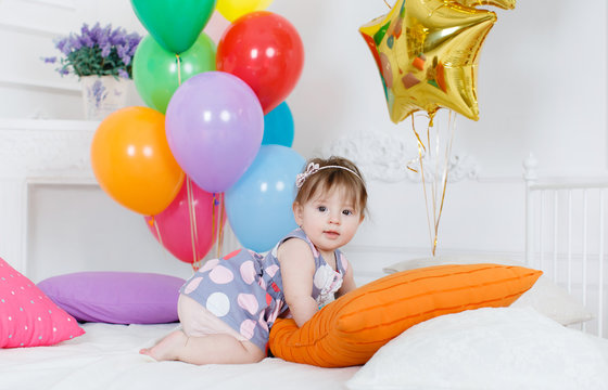 Portrait of a little redheaded girl with gray eyes,pink bow on its head, in a beautiful dress on a background of Golden stars and colorful balloons, posing in her first birthday on white background