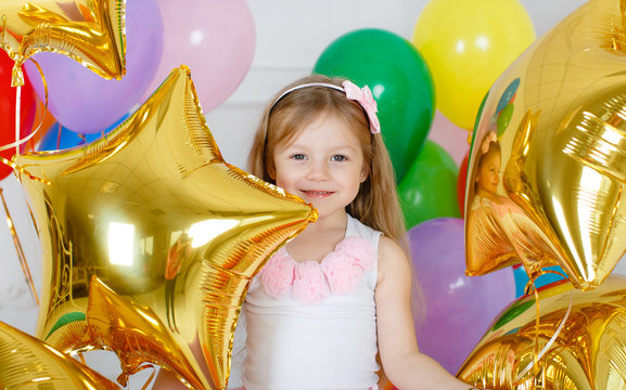 Little girl with long straight hair, with a pink bow on her head, dressed in a pink and white dress on gray background with colorful balloons and gold stars to your fourth birthday