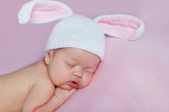 Peaceful sleep of a newborn baby on a pink bed,cute baby in hat with Bunny ears, sleeping sweetly tucked arms and legs on a pink background