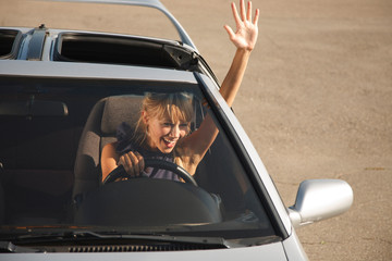 Cheerful girl in car is waving her hand