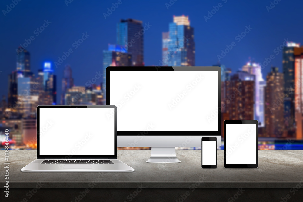 Poster Computer display, laptop, tablet and smart phone responsive display devices on table. Isolated white screen for mockup presentation. Cityscape in background