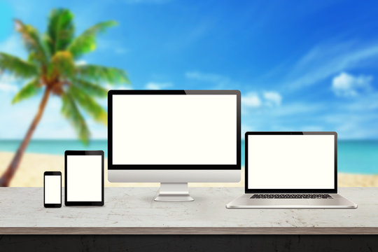 Computer display, laptop, tablet and smart phone responsive display devices on table. Isolated white screen for mockup presentation. Summer beach in background