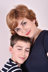 Mother and son with head to head smiling and hugging each other. Son with his eyes closed and mother looking at the camera.
