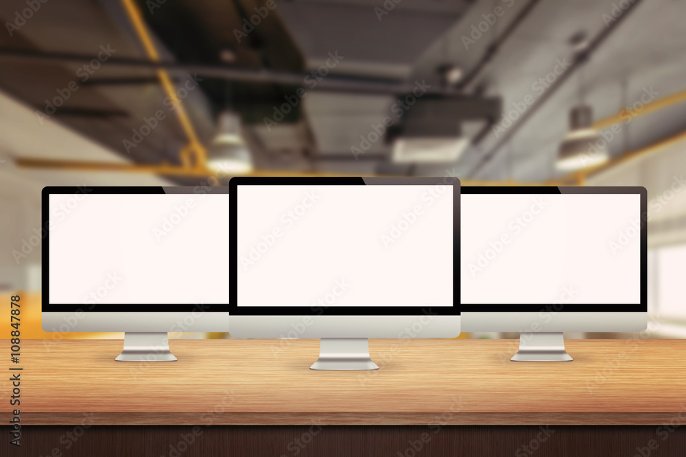 Aufkleber Three computer displays on table in office interior. Isolated white screen for mockup presentation