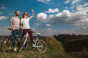 Obraz premium Beautiful young couple in love walking with bicycles, looking towards the beautiful nature and the blue sky. The concept of active rest