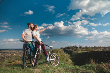Obraz premium Beautiful young couple in love walking with bicycles, looking towards the beautiful nature and the blue sky. The concept of active rest