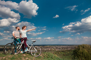 Beautiful young couple in love walking with bicycles, looking towards the beautiful nature and the blue sky. The concept of active rest