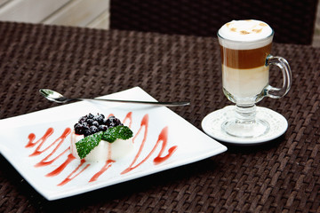Latte and panna cotta with berry sauce and mint leaves in a cafe.