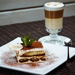Beautiful piece of delicious tiramisu with fresh mint and chocolate chip  and latte in a cafe.