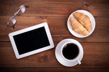 Tablet computer croissants cup of coffee glasses on a wooden background. Top view .