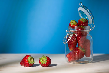 Strawberries on a table and a glass jar full of strawberries