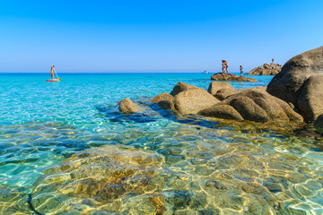Crystal clear sea water of Bodri beach and woman swimming on surfboard in distance, Corsica island,...