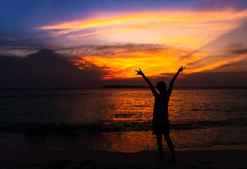 Silhouette of young woman spreading hand and relaxing on the bea