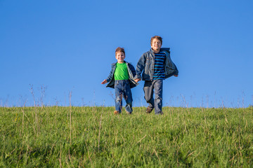 Naklejka na ściany i meble Two boys running together on green hill