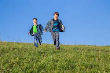 Two boys running together on green meadow