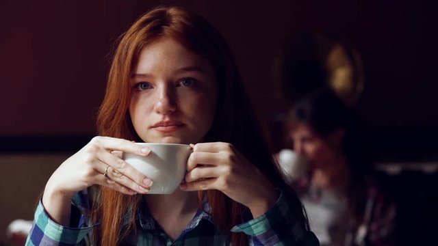 Pensive, thoughtful beautiful girl drinking coffee in cafe. Slow motion