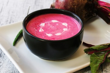 Beetroot soup in a black bowl with cream heart garnish