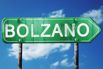 Bolzano road sign, vintage green with clouds background