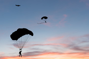 Silhouette of parachute and airplane on sunset background