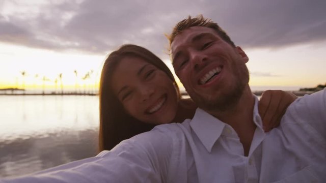 Couple romantic selfie video at sunset happy in love on beach embracing looking at camera enjoying travel vacation with ocean view. Mixed race couple on Big Island, Hawaii, USA. RED EPIC.