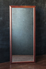 Classic rectangular mirror withot reflection standing In the empty room with black wall.