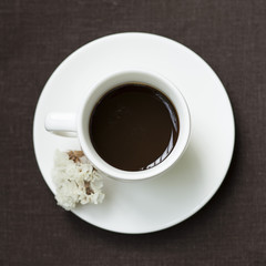 Cup of coffee with white flower on a brown tablecloth