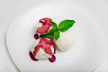 Three scoops of ice cream with strawberry syrup and mint on a white plate, white background, close-up, top view
