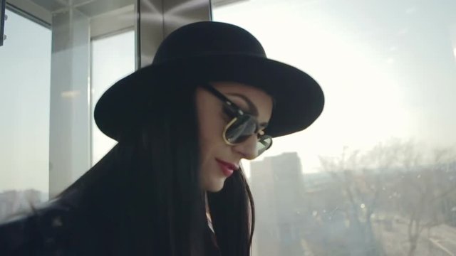 Portrait of beautiful model in black hat with glasses from the sun by the window - slow motion