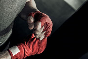 Closeup male hand of boxer with red boxing bandages. Fists of fighter before the fight or training in sport gym.