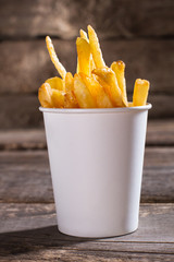 French fries in paper cup. Fries on brown wooden background. Size of portion in cafe. Free snack...