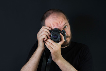     Man on black background in low key, holding analog camera and taking photos 