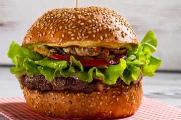 Big burger with sesame buns. Burger laying on bright napkin. Beefburger on white wooden background. Best dish in local cafe.
