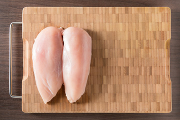 Raw chicken breasts and spices on wooden board
