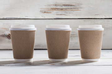 Ripple cups with lids. Three ripple paper cups. White wooden table with cups. Different grades of coffee.