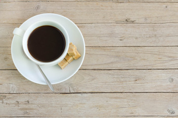 Cup of coffee with brown lump sugar on wooden table, top view