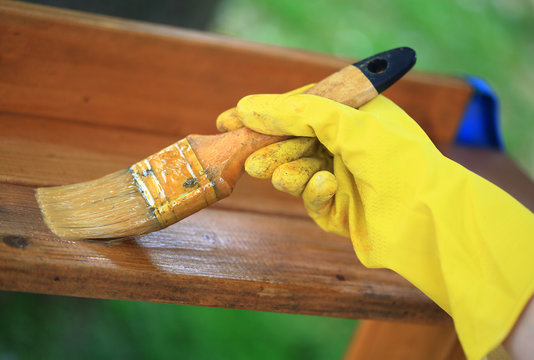 Gloved hand varnishing plank outdoor