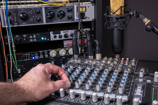 Engineer adjusting level settings on mixing console in recording studio setting.
