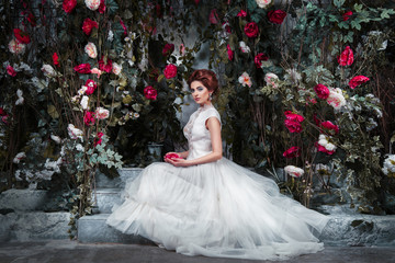 Luxury bride is sitting on the terrace in the mysterious garden of roses twined