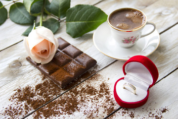 Marriage proposal with gold ring in the red hearth box.
Peach-colored rose, Turkish coffee and slices of chocolate on the wooden table
