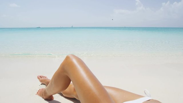 Sexy woman on beach in summer hat and bikini sitting in sand sunbathing. Beautiful unrecognizable girl on vacation travel on amazing perfect white powder sand beach with turquoise ocean. RED EPIC.