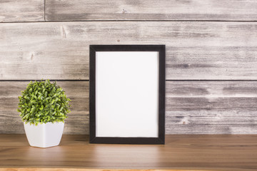Blank frame and plant on wood - obrazy, fototapety, plakaty